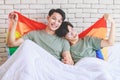 Two Asian cheerful lovely pride male gay men lover couple partner smiling sitting holding hands together in bed under colorful Royalty Free Stock Photo