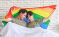 Two Asian cheerful lovely pride male gay men lover couple partner smiling sitting holding hands together in bed under colorful Royalty Free Stock Photo