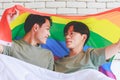 Two Asian cheerful lovely pride male gay men lover couple partner smiling sitting holding hands together in bed under colorful Royalty Free Stock Photo