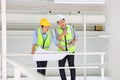 Two Asian contracting engineers wearing safety equipment while inspecting and discussing inside the warehouse