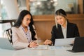 Two Asian female accountants working in the office with laptop computers and financial documents on the table.