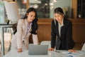 Two Asian female accountants working in the office with laptop computers and financial documents on the table.