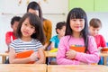 Two Asian girl kid hugging book and smiling in classroom and while teacher teach friends beside them,kindergarten education Royalty Free Stock Photo