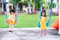 Two Asian girls are having fun swinging back and forth. Cute kids wear yellow outfits to play on the playground in the summer or Royalty Free Stock Photo