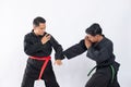 Two Asian men wearing pencak silat uniforms fight with punching and tangkisan bawah movements