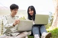 Two Asian university students are collaborating on work while sitting on the grass in the park Royalty Free Stock Photo