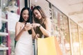 Two asian woman standing at store front with happy watching smart phone at shopping mall center. Royalty Free Stock Photo