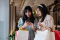 Two Asian women chat happily in a shopping mall corridor, looking at a smartphone together Royalty Free Stock Photo