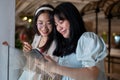 Two Asian women chat happily in a shopping mall corridor, looking at a smartphone together Royalty Free Stock Photo