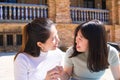 Two asian women holding a crytocurrency in their hands. One of the Asian women gives the coin to the other Asian woman. The