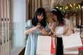 Two Asian women stand together in a shopping mall corridor, looking at a smartphone Royalty Free Stock Photo