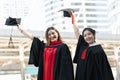 Two Asian young beautiful graduate female students with master and bachelor degree holding black cap with red tassels up to sky Royalty Free Stock Photo