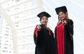 Two Asian young beautiful graduate female students with master and bachelor degree standing smiling and holding diploma in hand Royalty Free Stock Photo