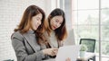 Two Asian young creative businesswomen holding a cup of coffee, working on laptop and disscuss about work while working in office Royalty Free Stock Photo