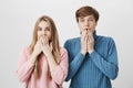 Two astonished horrified young students in stylish sweaters staring at camera in full disbelief, keeping mouths opened