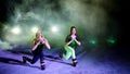 Two athletic women, doing various fitness exercises with weighting on their legs, At night, in light smoke, fog, in