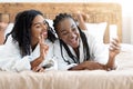 Two attractive black ladies taking selfie in bed