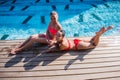 Two attractive blonde and brunette girls with long hair are lying on flor near pool. They wear bikini and swimsuit. They Royalty Free Stock Photo