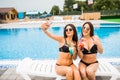Two attractive brunette women wearing bikini posing near the swimming pool, making selfie photo. Summer time Royalty Free Stock Photo