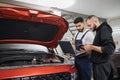 Two attractive mechanics men standing and looking at laptop with tablet and under car hood, Royalty Free Stock Photo