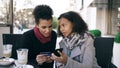 Two attractive mixed race women having online shopping with credit card and smartphone while talking and drinking coffee Royalty Free Stock Photo