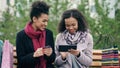 Two attractive mixed race women with paper bags sitting on bench and using tablet computer and credit card for online Royalty Free Stock Photo