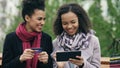 Two attractive mixed race women with paper bags sitting on bench and using tablet computer and credit card for online Royalty Free Stock Photo