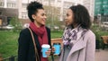 Two attractive mixed race women with shopping bags drinking coffe and talking at the street. Young girls smiling and Royalty Free Stock Photo