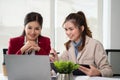 Two Asian businesswomen are looking at a laptop screen, discussing and planning work Royalty Free Stock Photo