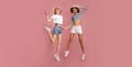 Two attractive young girls in summer clothes jumping on pink background, panorama Royalty Free Stock Photo