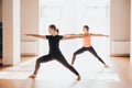 Two attractive young women balancing and practicing yoga in a light studio. Well being, wellness concept. One of the woman is plus