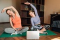 Two attractive young women doing stretching, yoga online at home. Self-isolation is beneficial, self-development and education on Royalty Free Stock Photo