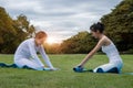 Two attractive young women folding blue yoga or fitness mat after working out at the garden. Healthy life, keep fit concepts.