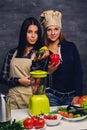 Two women preparing vegan vegetable juice with blender.