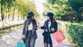 Two attractive young women are walking from shops along beautiful street carrying paper bags with purchases and talking Royalty Free Stock Photo