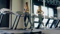 Two attrractive women doing cardion on treadmill in gym.