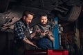 Two auto mechanic in a uniform, working on a workbench while standing under lifting car in the repair garage. Royalty Free Stock Photo