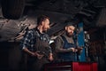 Two auto mechanic in a uniform, working on a workbench while standing under lifting car in the repair garage. Royalty Free Stock Photo