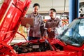 Two auto mechanics analyzing a vehicleÃ¢â¬â¢s engine using a laptop in a professional workshop. Modern automotive repair with Royalty Free Stock Photo