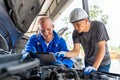 Two auto mechanics using a computer tablet while working together on the car engine at car repair garage Royalty Free Stock Photo