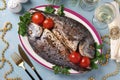 Two baked fish dorado with spice serwed with parsley and cherry tomatoes on plate on light blue background. Top view Royalty Free Stock Photo