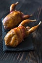 Two baked quails wrapped in bacon on the black stone board
