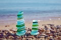 Two balanced pyramids of sea pebbles polished blue and green bottle glass against background of oncoming sea wave Royalty Free Stock Photo