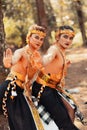 Two Balinese men dancing together in front of the tree while wearing a golden crown and golden necklaces in stripped clothes Royalty Free Stock Photo