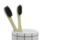 Two bamboo black bristle toothbrushes in cup isolated on white background.