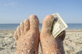 Two bare feet of caucasian woman soiled in sand with shell rock and dollar Royalty Free Stock Photo