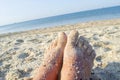 Two bare feet of caucasian woman soiled in sand with shell rock on sandy sea Royalty Free Stock Photo