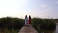 Two barefoot women from behind is walking on wooden trail to the lake