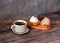 Two basket cakes with cream and a cup of black coffee on a saucer with a spoon on a wooden table Royalty Free Stock Photo