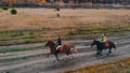 Two bay horses with equestrians on their back are galloping on the autumn field Royalty Free Stock Photo